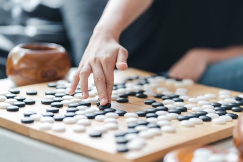 Spielerhand setzt Stein auf ein Go-Brett - ein antikes Spiel, das auch als Baduk in Korea, als Weiqi in China oder als Igo in Japan bekannt ist.
