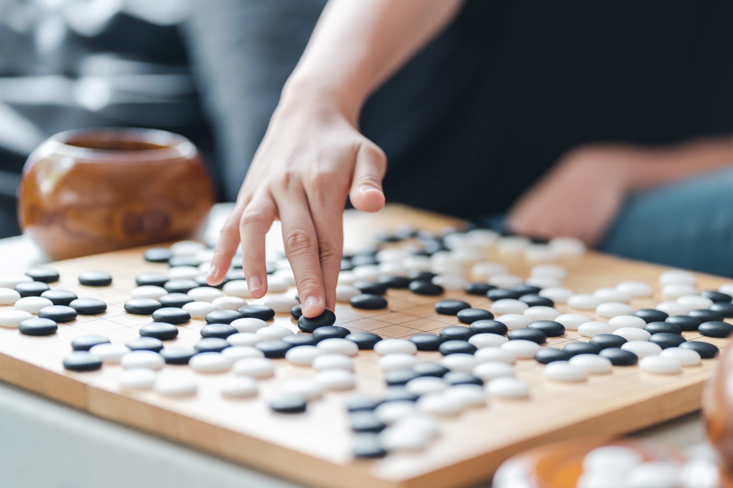 hand putting baduk black stone on wooden grid board - an ancient game also known as baduk in Korean, weiqi in Chinese and Igo in Japanese